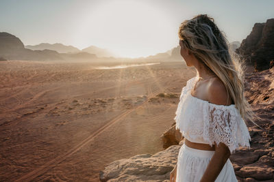 Rear view of young woman standing on desert against sky