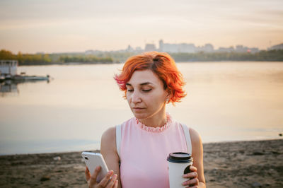 Mid adult woman using mobile phone while standing by river against sky