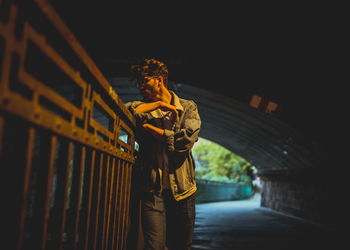 Young man leaning on railing while looking away in tunnel