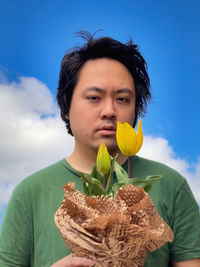 Portrait of beautiful woman holding flower against sky