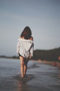 Rear view of woman walking on beach against clear sky