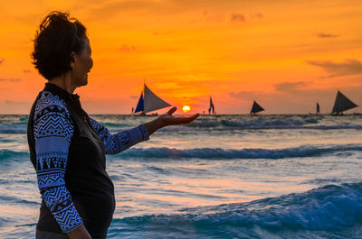 Woman standing on beach against sky during sunset