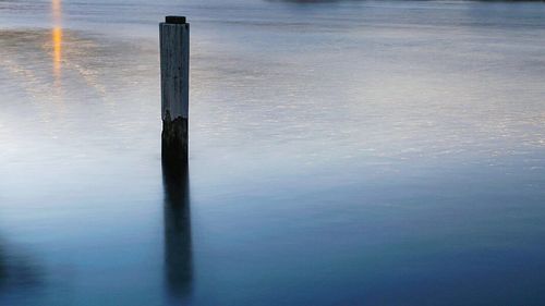 Wooden post in lake during sunset