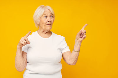 Portrait of young woman gesturing against yellow background