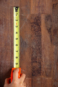 Cropped hand of woman holding measuring tape on wooden table