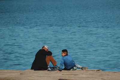 Man and teenage boy sitting against lake