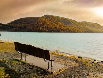 Bench by lake against sky