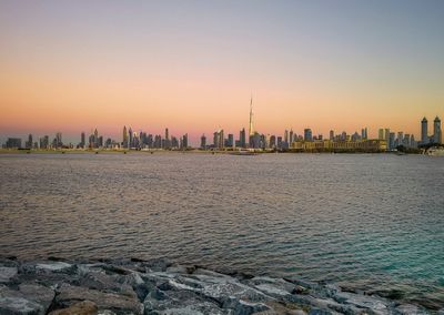 Sea by buildings against sky during sunset