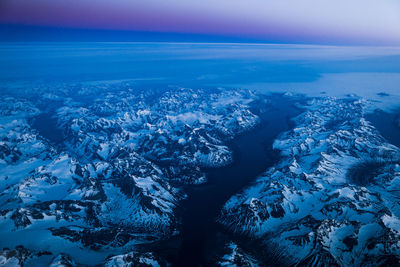 Aerial view of sea and snow covered mountains against blue sky