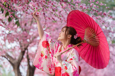 Woman with pink flower standing against trees