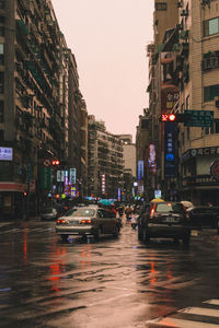 Cars on wet road against sky in city