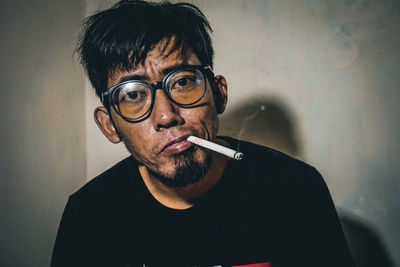 Portrait of man smoking cigarette against wall