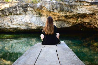 Rear view of woman sitting on pier against cave in sea