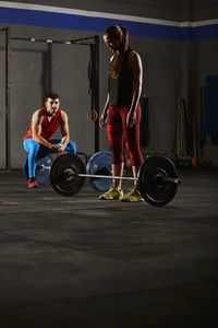 Full length of woman standing by barbell at gym