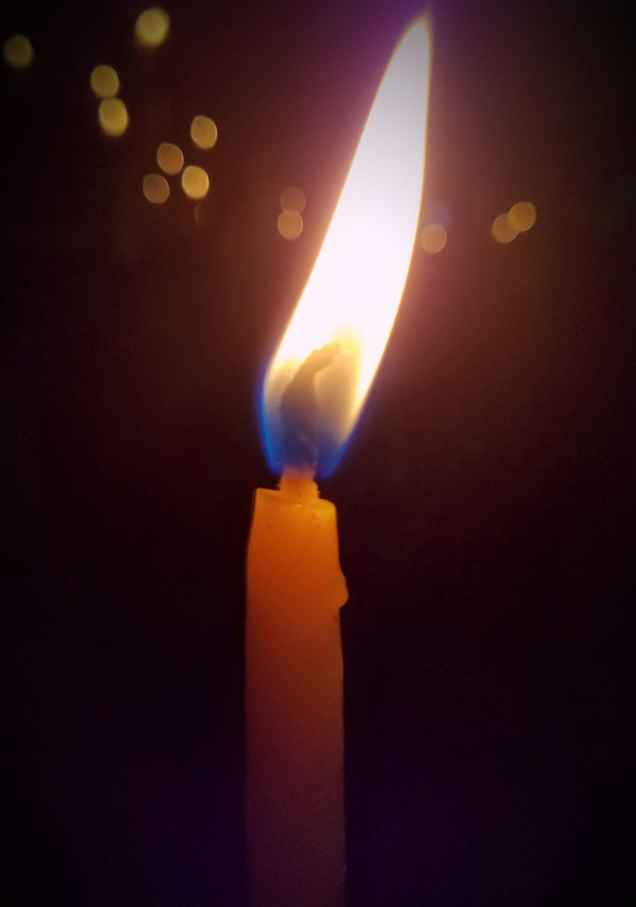 CLOSE-UP OF LIT CANDLE IN DARK