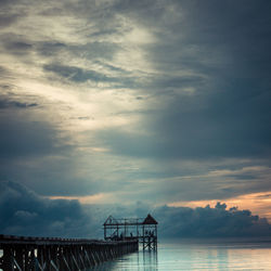 Silhouette bridge over sea against sky during sunset