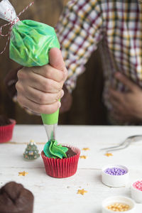 Midsection of man preparing cupcake on table