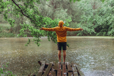 Rear view of man standing by tree in lake