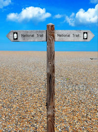 Sign board on beach against sky