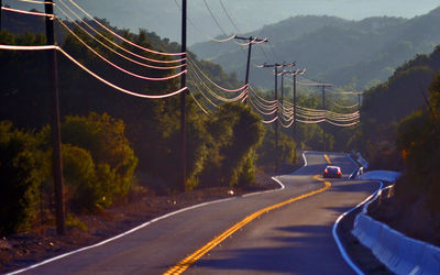 Electric poles by country road against tree mountain