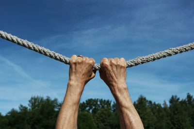 Cropped image of man hand holding rope against sky