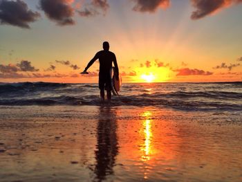 Rear view of silhouette man with surfboard walking in sea at sunset