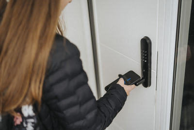Midsection of girl unlocking door lock through smart phone while standing at home