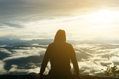 Rear view of man sitting on mountain against sky