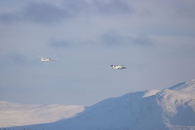 Low angle view of airplanes flying over snowcapped mountains against sky