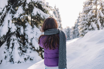 Rear view of woman standing against trees during winter