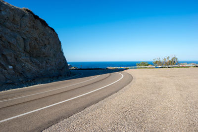 Surface level of road by sea against clear blue sky