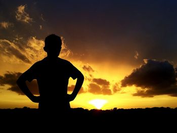 Silhouette man with hand on hip standing against sky during sunset