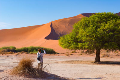 Rear view of mature woman photographing while standing by sand dune in desert