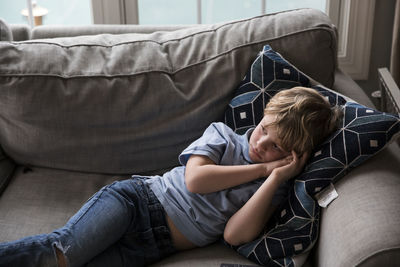 Sad blonde boy watches tv while laying on couch