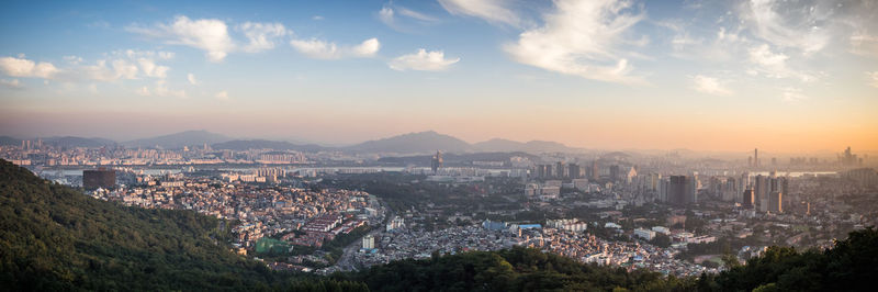 Panoramic view of cityscape by mountains against sky during sunset