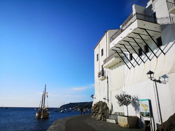 Buildings by sea against clear blue sky