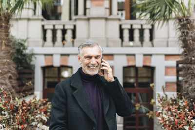 Portrait of man holding smart phone while standing against building