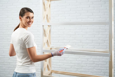 Portrait of smiling young woman standing against wall