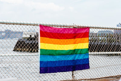 Rainbow flag hanging on chainlink fence against sky