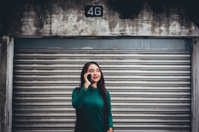 Woman talking on phone while standing by shutter