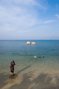 Rear view of man standing on beach against sky