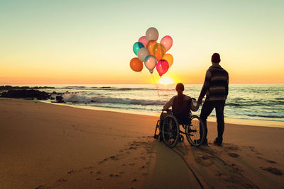 Rear view of people enjoying on beach during sunset