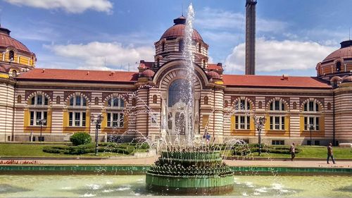 Fountain in front of building against sky