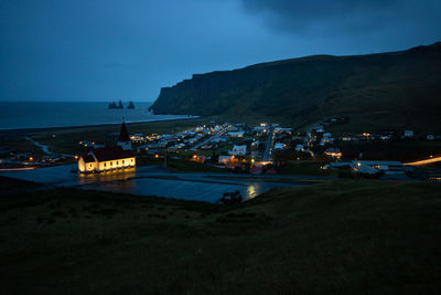 Illuminated buildings on field by mountain at night