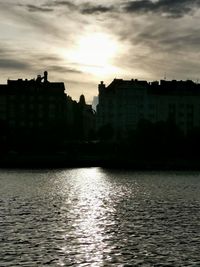 Buildings by river against sky during sunset