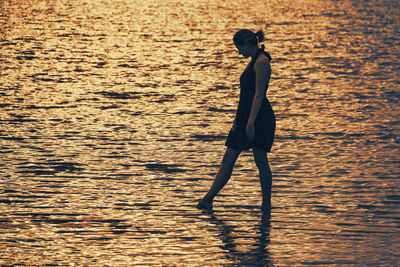 Silhouette woman standing at beach during sunset in the sea