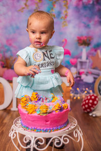 Close-up of cute baby girl standing in front on birthday cake