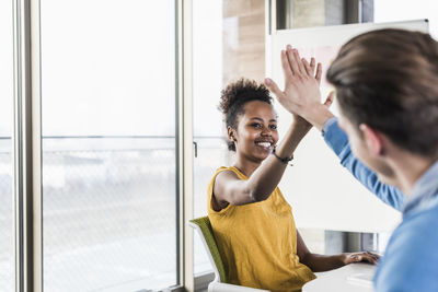 Happy young woman high fiving with colleague in office
