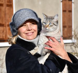 Smiling mature woman wearing warm clothing while carrying cat in city