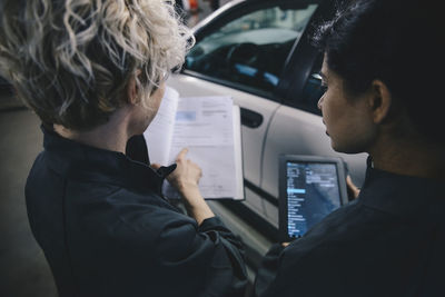 High angle view of female explaining coworker over diary in auto repair shop